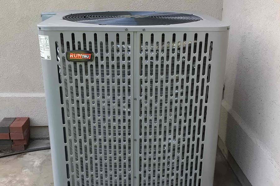 Outdoor air conditioning unit installed next to a stucco wall, positioned on a concrete pad.