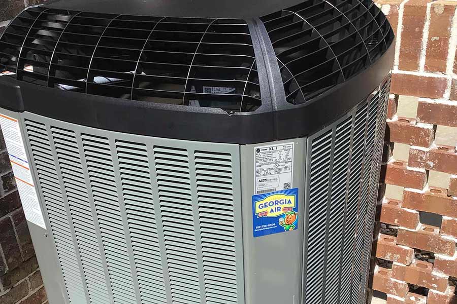 Outdoor HVAC unit installed against a brick wall, featuring a Georgia Air service sticker