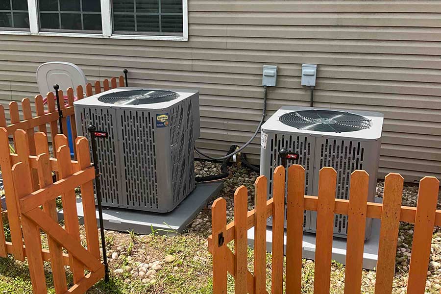 Two outdoor HVAC units enclosed by a wooden fence