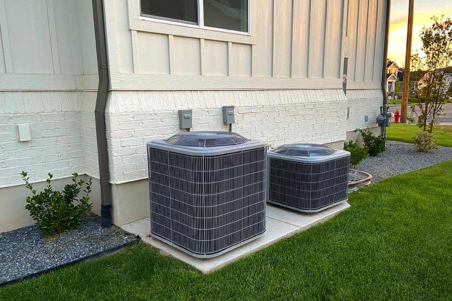 Two outdoor air conditioning units installed side by side on a concrete pad next to a house