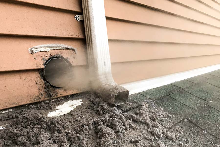 A dryer vent on the exterior wall of a house expelling lint buildup onto the roof
