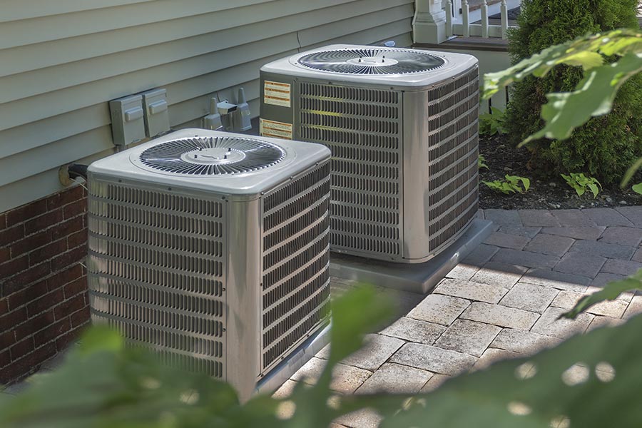 Two outdoor AC units beside a house on a paved patio